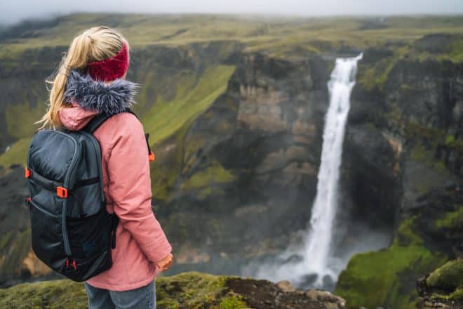 Woman with backpack and lilac jacket enjoying Haifoss waterfall of Iceland Highlands