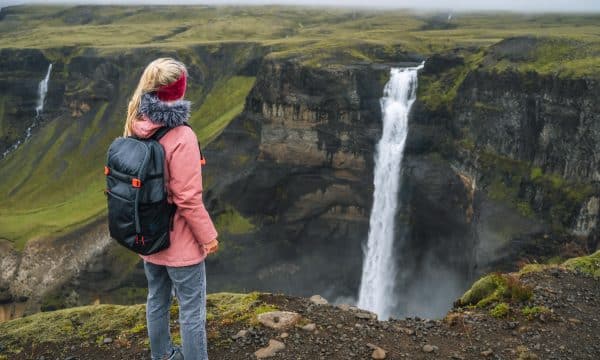 Mujer con mochila y chaqueta lila disfrutando de la cascada Haifoss de las Tierras Altas de Islandia