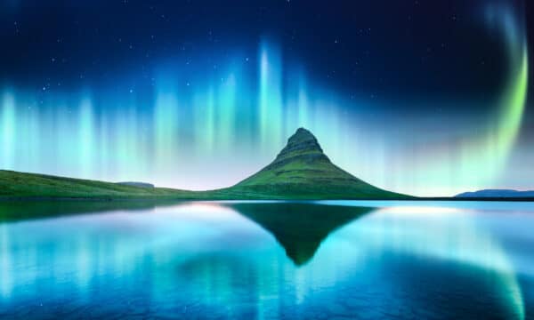Green Northern Lights behind Mt Kirkjufell in Iceland and reflecting in the lake in front of it.