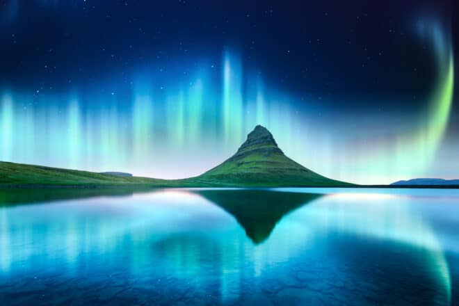 Green Northern Lights behind Mt Kirkjufell in Iceland and reflecting in the lake in front of it.