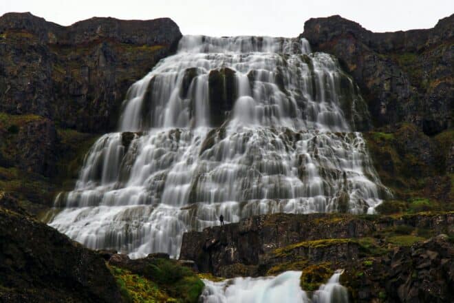 Un hombre parado frente a la cascada Dynjandi en Islandia