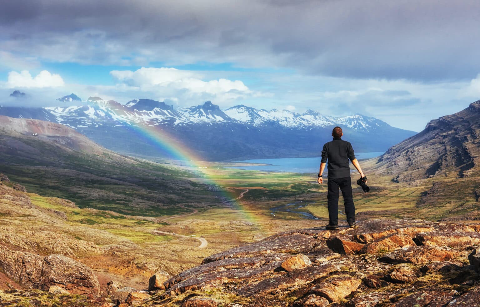 Un homme à Landmannalaugar, Islande regardant des montagnes bleues et un arc-en-ciel