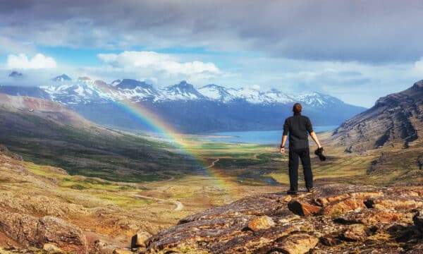 Un hombre en Landmannalaugar, Islandia mirando montañas azules y un arco iris