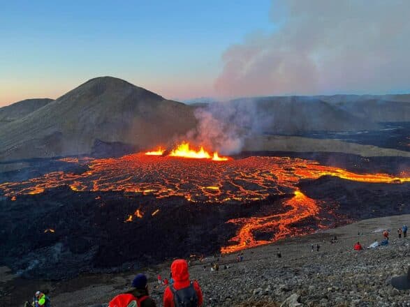 People in a hill looking at red lava flowing from a volcano in Iceland