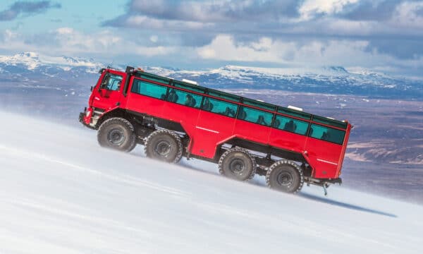 Un gros camion rouge qui monte un glacier en Islande avec des montagnes en arrière-plan.