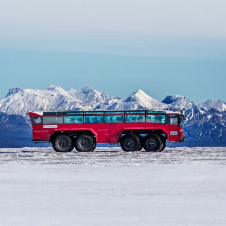 A red glacier truck on top of a glacier in Iceland with blue mountains in the background.
