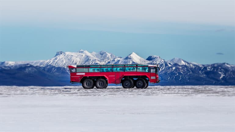 A red glacier truck on top of a glacier in Iceland with blue mountains in the background.