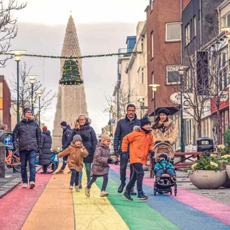Una familia caminando por una calle arcoiris bajo adornos navideños en Reykjavik, Islandia.