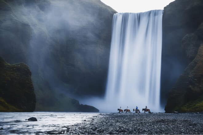 Cuatro jinetes sobre caballos islandeses frente a la cascada de Skógafoss