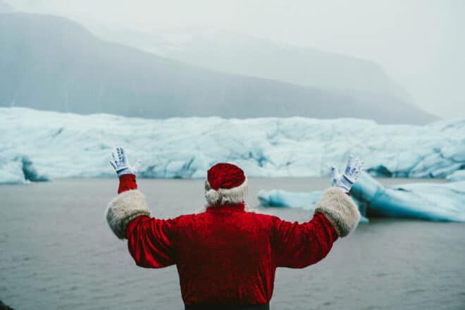 A man in a Santa Claus outfit in front of Jökulsárlón Glacier Lagoon in Iceland.