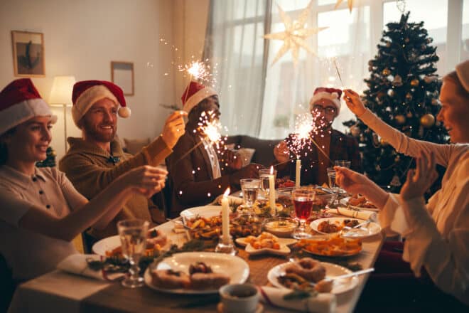 Multi-ethnic group of people raising glasses while enjoying Christmas dinner at home