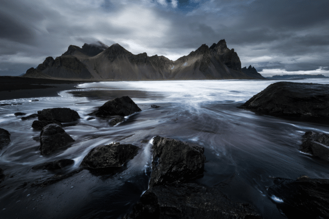 A black sand beach in front of Vestrahorn mountain with clouds overhead in Iceland.