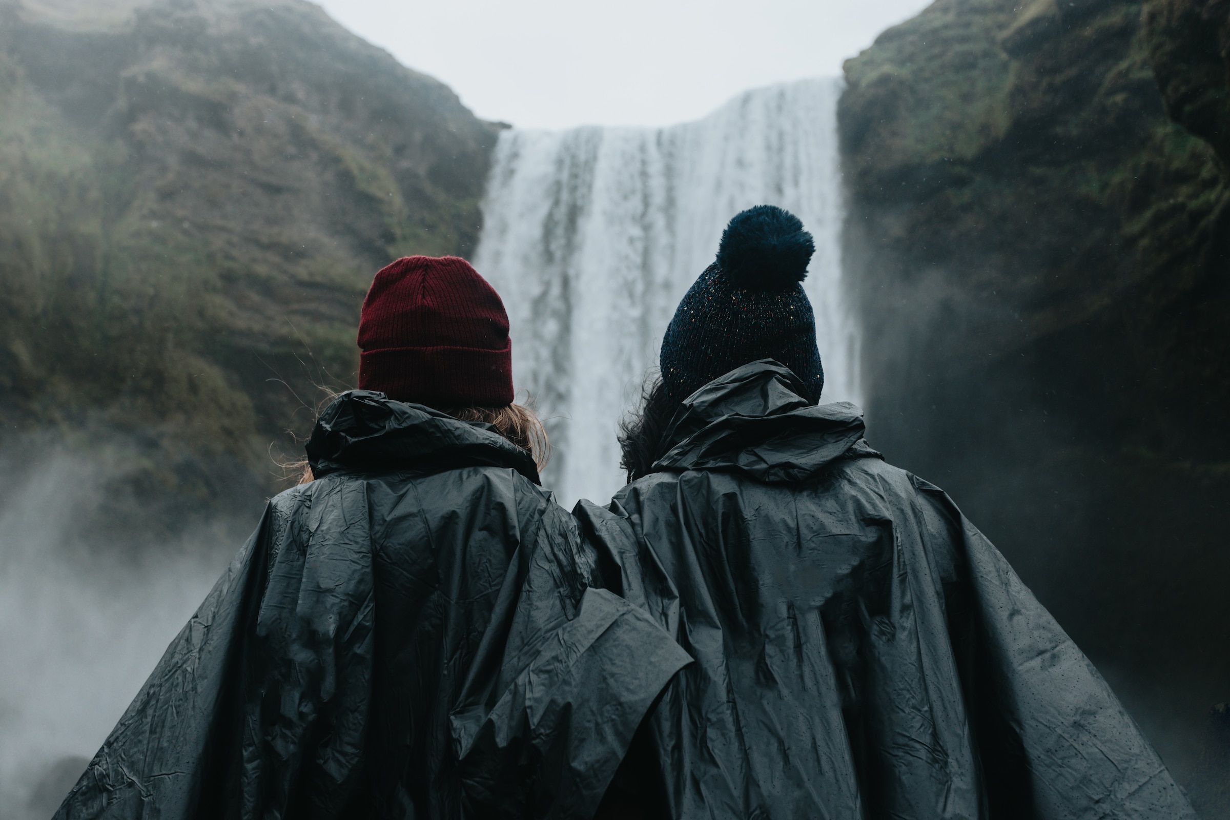 Woman couple in rain clothes in front of Skógafoss waterfall in Iceland during a moody day.