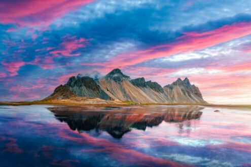 Montagne Vestrahorn dans le sud de l'Islande avec un ciel bleu et rose reflété dans la mer ci-dessous.