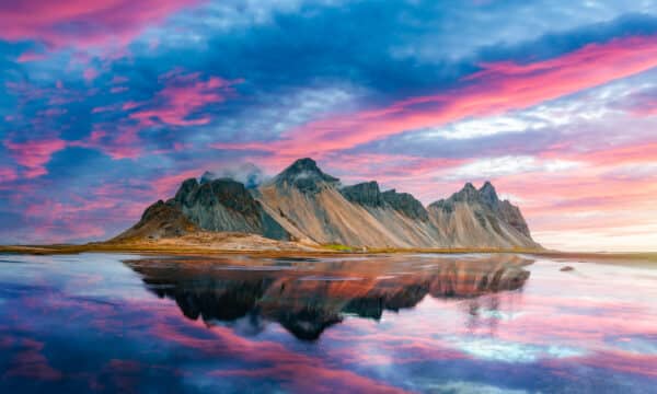 Montaña Vestrahorn en el sur de Islandia con cielos azules y rosas reflejados en el mar.