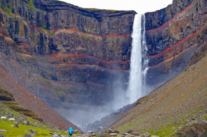 La alta cascada de Hengifoss en el este de Islandia en el verano, un hombre parado frente a ella.