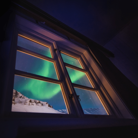 Les aurores boréales et la montagne enneigée à travers une fenêtre en Islande