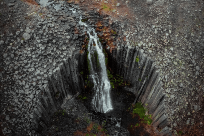 Des milliers de colonnes de basalte géométriques entourant une chute d'eau dans l'Est de l'Islande