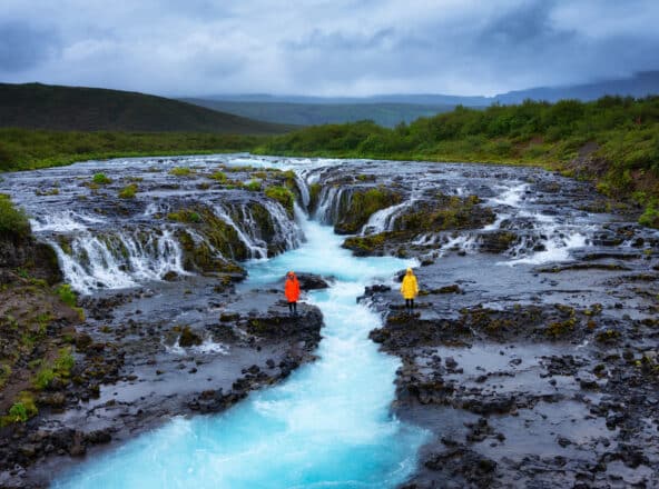 Dos personas suplentes en el lado opuesto de la cascada Brúarfoss en el sur de Islandia