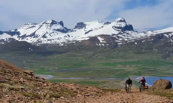 Montagnes enneigées de l'Est de l'Islande à l'arrière avec un homme et un VTT sur un chemin de gravier devant.