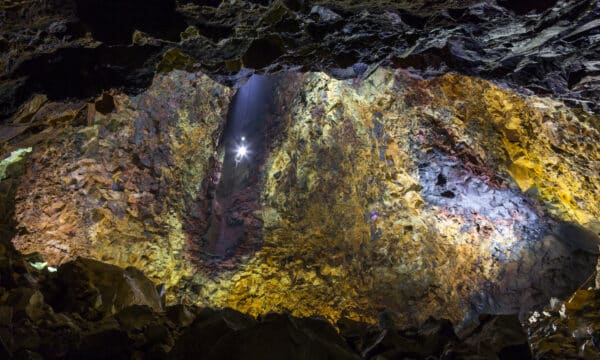 Un ascenseur descendant dans une vaste chambre magmatique aux murs jaunes, bleus et violets d'un volcan endormi en Islande.