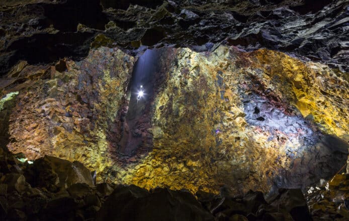 An elevator descending into a vast magma chamber with yellow, blue and purple walls of a dormant volcano in Iceland.