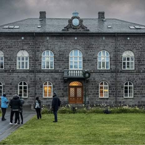 Des gens devant le bâtiment du Parlement islandais par temps nuageux.