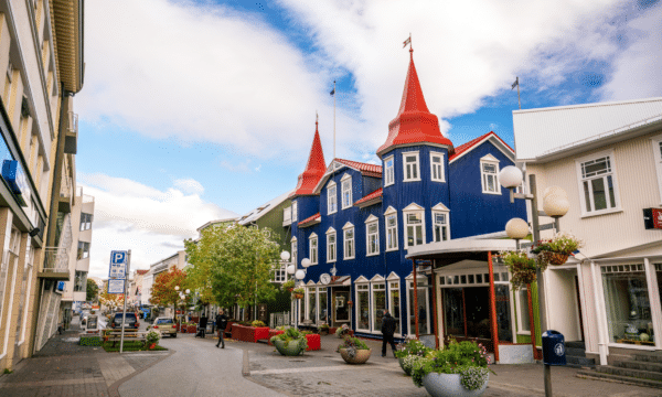 A street view of Akureyri, North Iceland with a blue house with a red roof in the foreground.