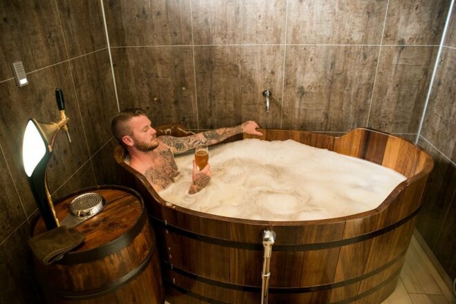 Un hombre sumergido en una tina llena de cerveza, sosteniendo un vaso de cerveza en el Beer Spa en el norte de Islandia