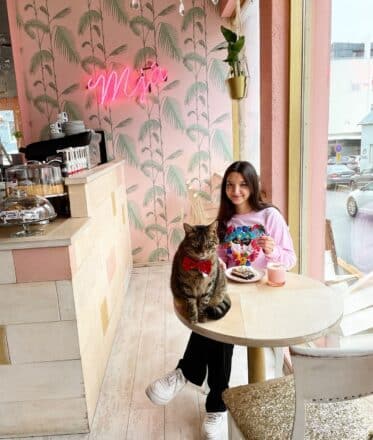 Una niña disfruta de un café y un pastel con un gato sentado en la mesa en Cat Cafe en Reykjavik.