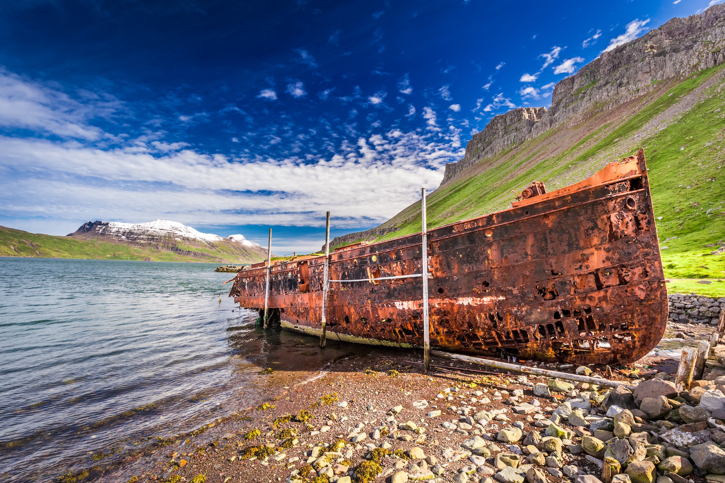 Ancienne épave sur une plage rocheuse avec des montagnes en arrière-plan dans le village de Djupavik dans les Westfjords, en Islande.