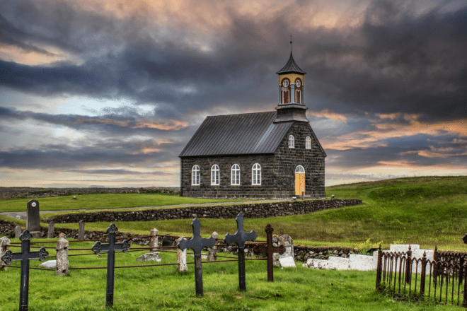 Iglesia Hvalsneskirkja en un día oscuro y nublado con cementerio en primer plano, Reykjanes, Islandia.
