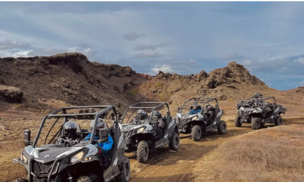 A row of buggy vehicles surrounded by dark volcanic cliffs near Lake Myvatn, Iceland.