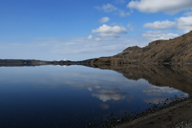 Lake Kleifarvatn in Iceland. Perfectly calm water with reflection of the mountains and sky. Blue sky in the background with white clouds.