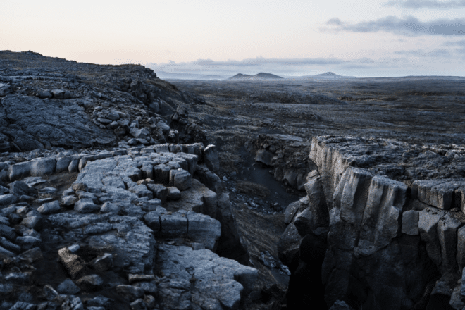 Dark walls of the Mid-Atlantic Ridge with mountains in the background on the Reykjanes Peninsula, Iceland.