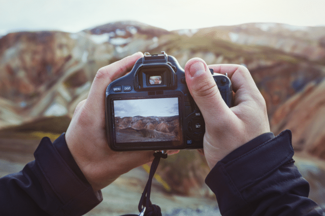 Photographer's hands holding camera, taking photo of mountains at Landmannalaugar, Iceland.