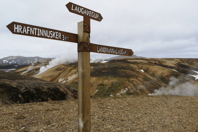 A sign on the Laugavegur Hike in the Icelandic Highlands, geothermal smoke and hills in the background.