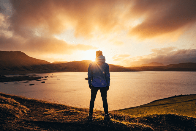 Man standing in blue jacket looking at spectacular sunset over frostadavatn lake in Landmannalaugar in Iceland.