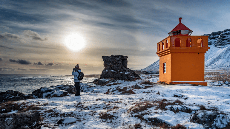 Una mujer fotografiando paisajes islandeses junto al faro de Hafnarnesviti.