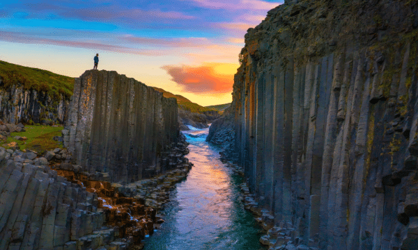 A man standing on a cliff at Studlagil Canyon in Iceland at sunset.