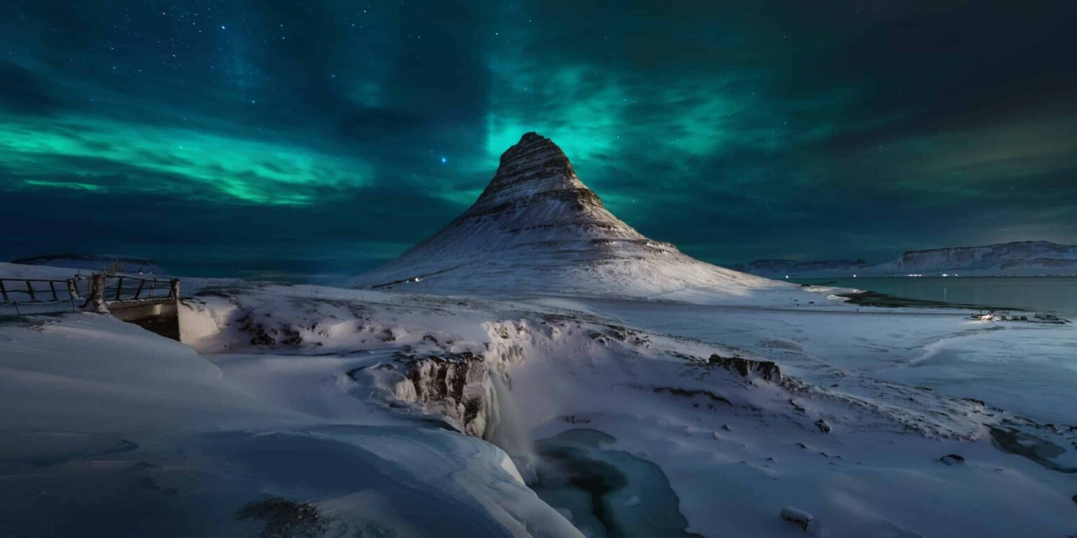 Una hermosa vista de la nieve que cubre el suelo y la colina kirkjufell bajo un cielo con Aurora en Islandia.