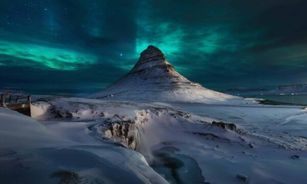 A beautiful view of the snow covering the ground and kirkjufell hill under a sky with Aurora in Iceland.
