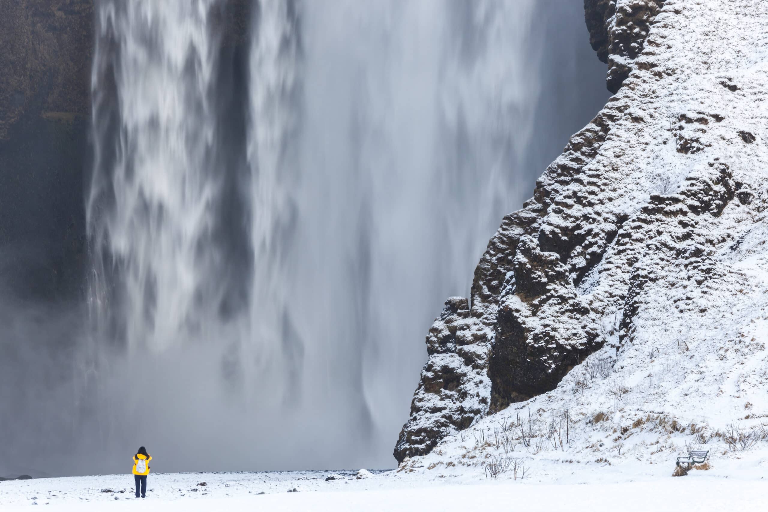 Une personne debout devant la cascade de Skógafoss en hiver.