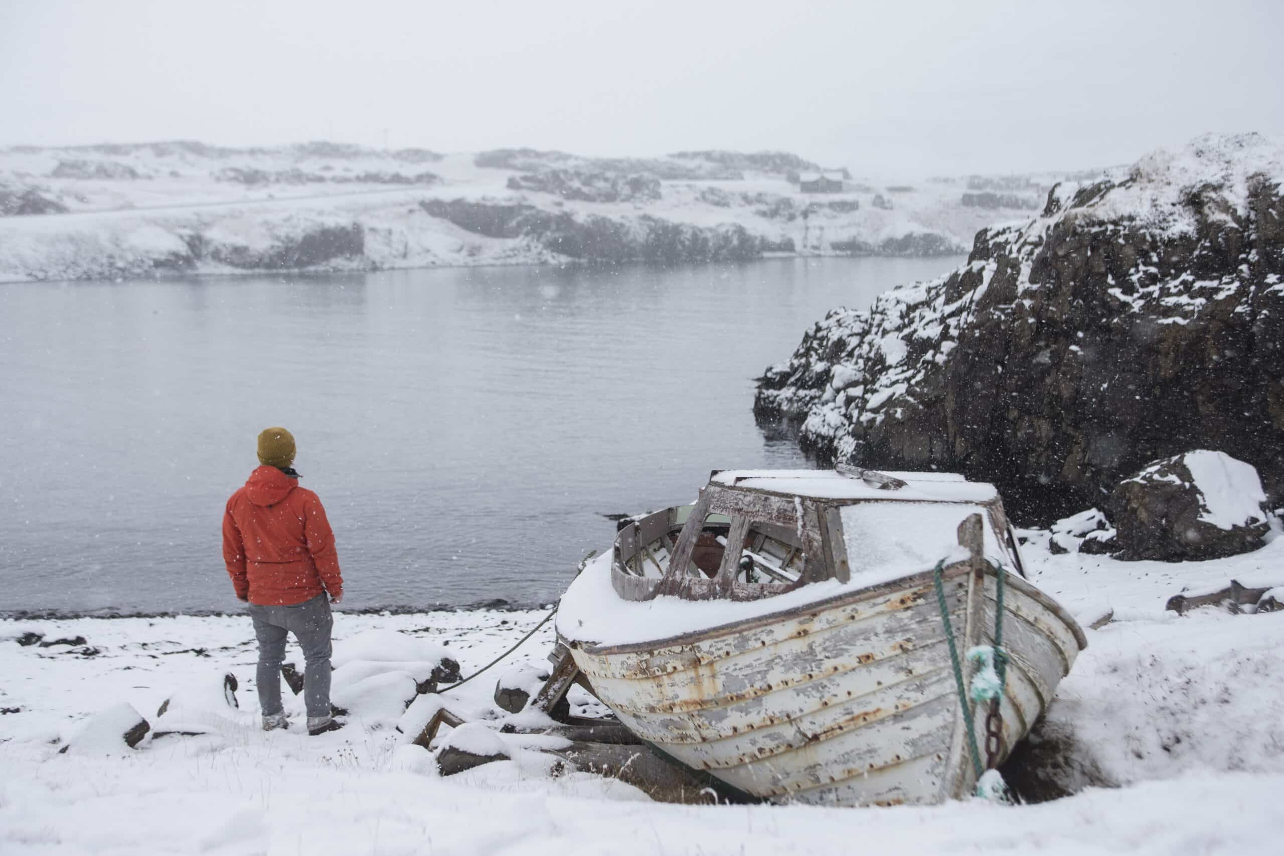 Un homme à côté d'un bateau au bord d'un lac en Islande, de la neige partout, une scène hivernale.