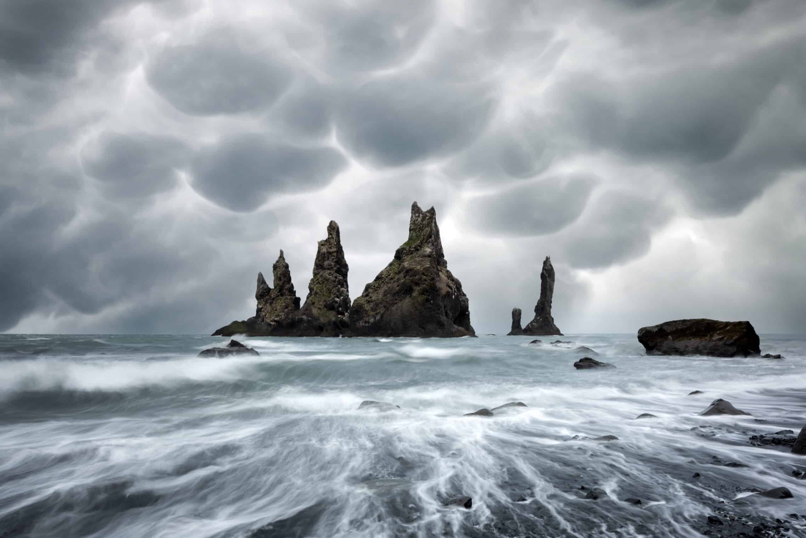 Formations rocheuses de basalte sur une plage noire avec un ciel orageux avec des nuages mammatus menaçants en arrière-plan. Reynisdrangar, Vik, Islande