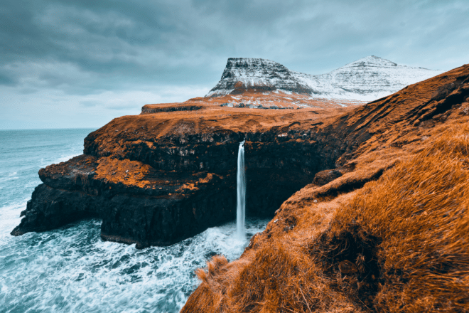 Chute d'eau de Mulafossur sur les îles Féroé en hiver avec une montagne enneigée en arrière-plan.