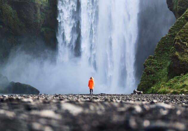 Een persoon voor de Skógafoss-waterval in Zuid-IJsland, in de zomer.