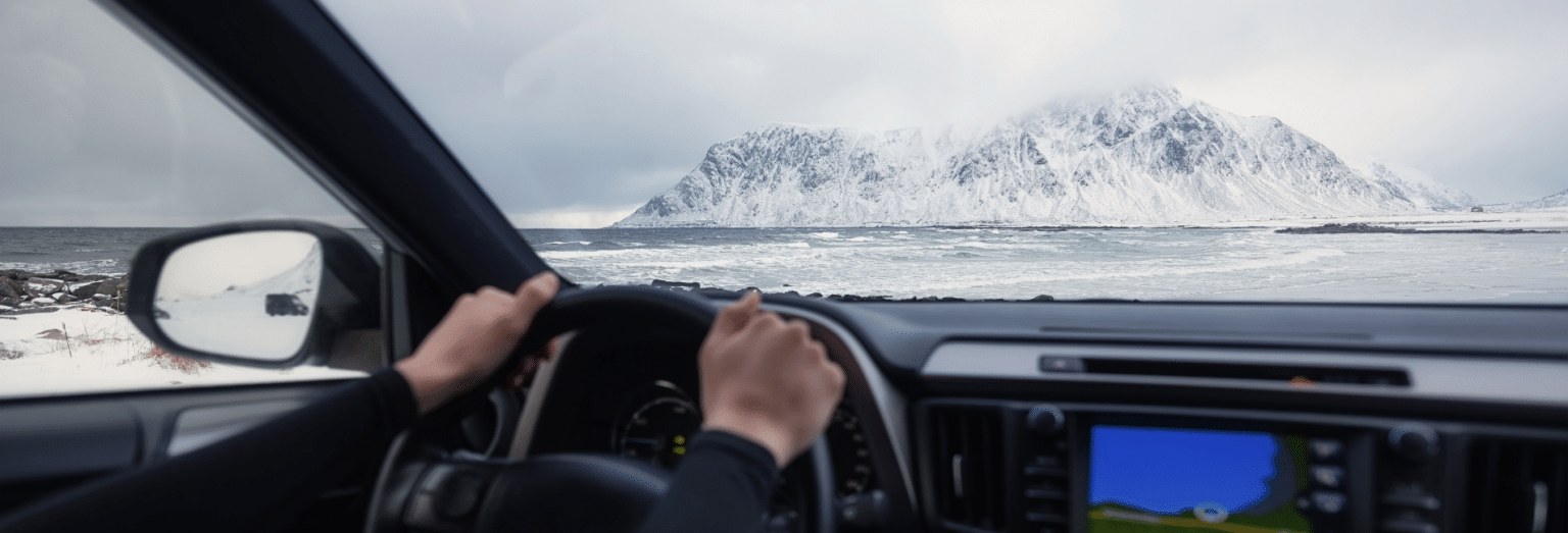 Hands on wheels inside a car, a view of a snowy mountain in Iceland in front.