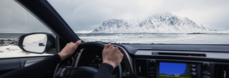 Les mains sur le volant d'une voiture, vue sur une montagne enneigée d'Islande au premier plan.