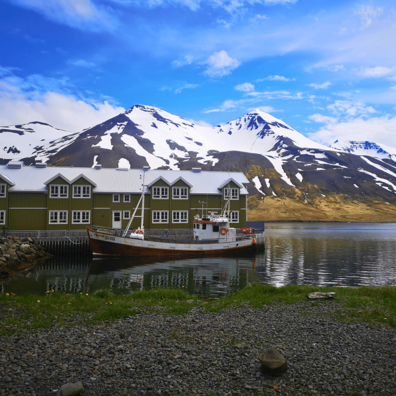 A boat in front of a green house in Siglufjörður, North Iceland. Snow-capped mountain in the background.
